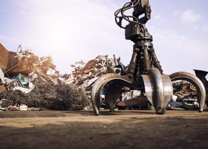 Metal junk yard with hydraulic lifting machine with mechanical grabber for scrap metal lifting.